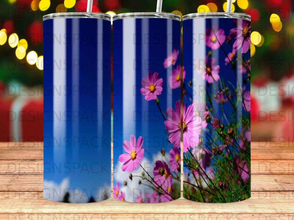 Pink cosmos flowers bloom against a blue sky on a tumbler.