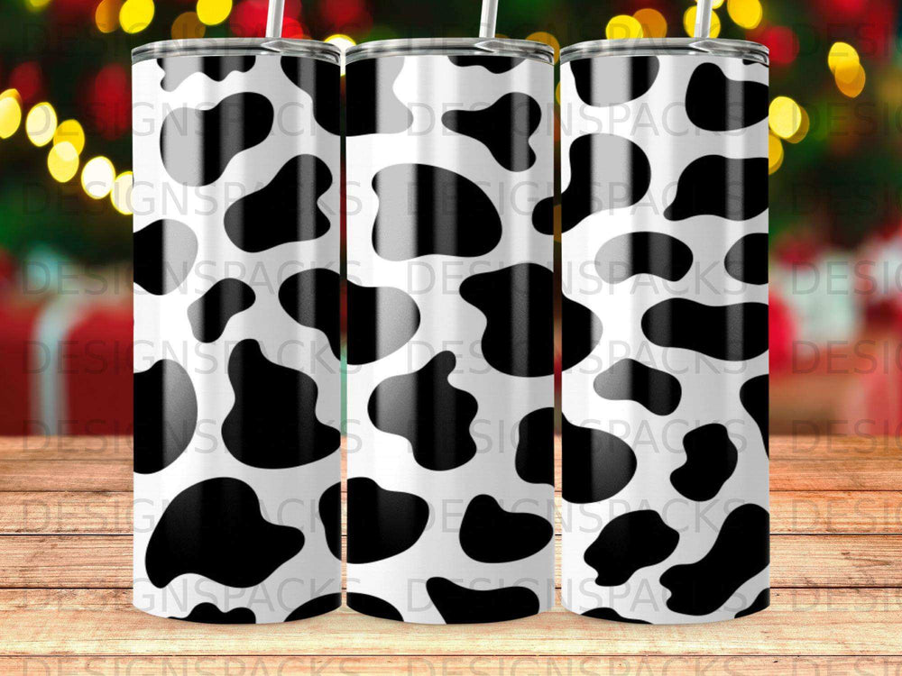 Cow print pattern on a cylindrical tumbler with blurred festive lights in the background.