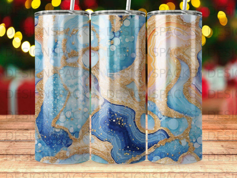 Blue and gold marbled tumbler with glitter accents and bokeh background.